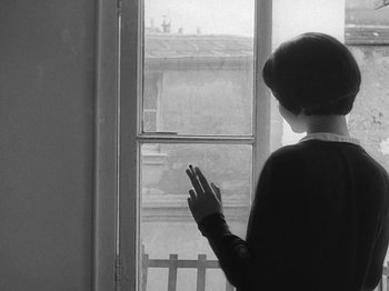Movie still from “My Life to Live” (1962), directed by Jean-Luc Godard – A woman standing in front of a window with her hand up; Medium shot, Low angle