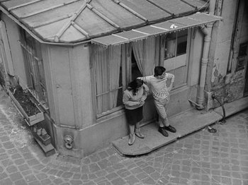 Movie still from “My Life to Live” (1962), directed by Jean-Luc Godard – A man and a woman standing in front of a window; Wide shot, High angle