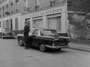 Movie still from “My Life to Live” (1962), directed by Jean-Luc Godard – A man standing next to an old car on the side of the street; Wide shot, Low angle