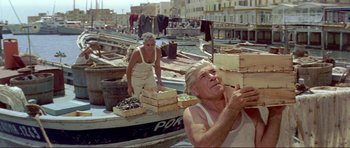 Movie still from “Von Ryan's Express” (1965), directed by Mark Robson – Two men are loading boxes on a boat in the water; Medium shot, Low angle