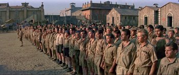 Movie still from “Von Ryan's Express” (1965), directed by Mark Robson – A large group of men standing next to each other in front of a building; Wide shot, High angle