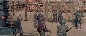 Movie still from “Von Ryan's Express” (1965), directed by Mark Robson – A group of men standing next to each other in a field; Wide shot, High angle