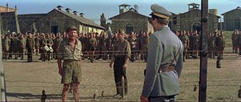 Movie still from “Von Ryan's Express” (1965), directed by Mark Robson – A group of men standing in front of a building; Wide shot, Over the shoulder angle