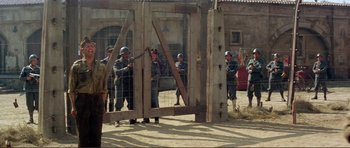Movie still from “Von Ryan's Express” (1965), directed by Mark Robson – A group of men standing next to each other in a fenced area; Wide shot, Over the shoulder angle