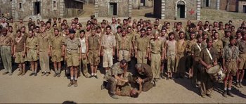 Movie still from “Von Ryan's Express” (1965), directed by Mark Robson – A large group of men standing around a man lying on the ground; Wide shot, High angle