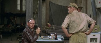 Movie still from “Von Ryan's Express” (1965), directed by Mark Robson – A man sitting at a table in a room with another man; Medium shot, Over the shoulder angle