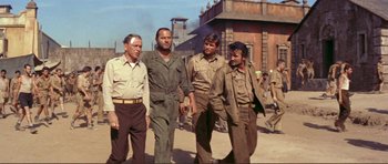 Movie still from “Von Ryan's Express” (1965), directed by Mark Robson – A group of men standing next to each other on a street; Medium shot, Low angle