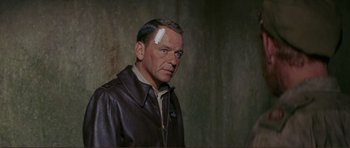 Movie still from “Von Ryan's Express” (1965), directed by Mark Robson – An older man wearing a leather jacket with a bandage on his head; Medium shot, Over the shoulder angle