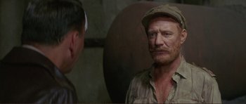 Movie still from “Von Ryan's Express” (1965), directed by Mark Robson – A man with a beard and a hat is standing next to another man; Close Up shot, Over the shoulder angle