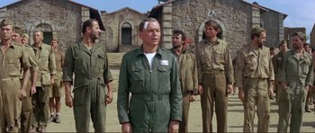 Movie still from “Von Ryan's Express” (1965), directed by Mark Robson – A group of men standing next to each other on top of a dirt field; Medium shot, Low angle