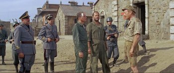 Movie still from “Von Ryan's Express” (1965), directed by Mark Robson – A group of men standing next to each other on a dirt field; Wide shot, Over the shoulder angle