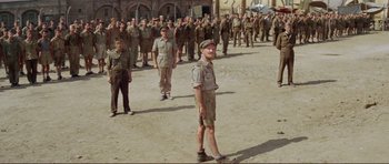 Movie still from “Von Ryan's Express” (1965), directed by Mark Robson – A group of men standing next to each other on a street; Wide shot, High angle