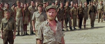 Movie still from “Von Ryan's Express” (1965), directed by Mark Robson – A group of men standing next to each other in the sand; Medium shot, Low angle