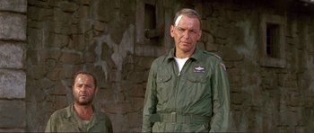 Movie still from “Von Ryan's Express” (1965), directed by Mark Robson – A man in a military uniform stands next to another man; Medium shot, Low angle