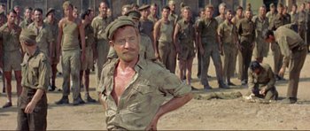 Movie still from “Von Ryan's Express” (1965), directed by Mark Robson – A man in a hat standing in front of a group of soldiers; Medium shot, Low angle