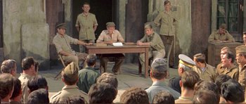 Movie still from “Von Ryan's Express” (1965), directed by Mark Robson – A group of men sitting at a table in front of an audience; Wide shot, High angle