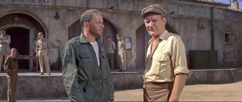 Movie still from “Von Ryan's Express” (1965), directed by Mark Robson – Two men standing next to each other in front of a building; Medium shot, Low angle