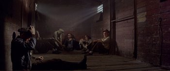Movie still from “Von Ryan's Express” (1965), directed by Mark Robson – A group of men sitting on the ground in front of a brick wall; Wide shot, High angle
