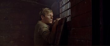 Movie still from “Von Ryan's Express” (1965), directed by Mark Robson – A man leaning up against a wall looking out a window; Close Up shot, Low angle