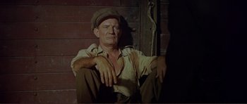 Movie still from “Von Ryan's Express” (1965), directed by Mark Robson – An old man sitting on the ground wearing a hat; Medium shot, High angle