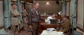 Movie still from “Von Ryan's Express” (1965), directed by Mark Robson – A man holding a gun standing in front of a table; Medium shot, Over the shoulder angle