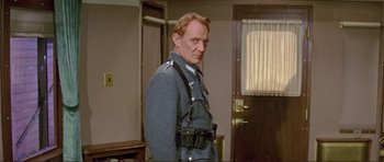 Movie still from “Von Ryan's Express” (1965), directed by Mark Robson – A man in a uniform standing in front of a door; Medium shot, Low angle