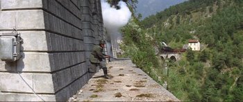 Movie still from “Von Ryan's Express” (1965), directed by Mark Robson – A man standing on the side of a building near trees; Extreme Wide shot, High angle