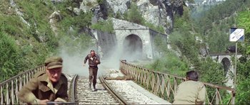 Movie still from “Von Ryan's Express” (1965), directed by Mark Robson – A man running across a train track next to a bridge; Wide shot, High angle