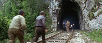 Movie still from “Von Ryan's Express” (1965), directed by Mark Robson – A man walking on train tracks next to a tunnel; Extreme Wide shot, High angle