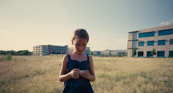 Movie still from “Voyage of Time” (2016), directed by Terrence Malick – A young girl in a field looking down at her cell phone; Wide shot, Low angle