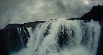 Movie still from “Voyage of Time” (2016), directed by Terrence Malick – A large waterfall is pouring into a body of water; Extreme Wide shot, Low angle