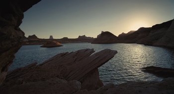 Movie still from “Voyage of Time” (2016), directed by Terrence Malick – The sun is setting over a lake with mountains in the background; Extreme Wide shot, High angle