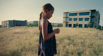 Movie still from “Voyage of Time” (2016), directed by Terrence Malick – A young girl in a field with buildings in the background; Wide shot, Over the shoulder angle