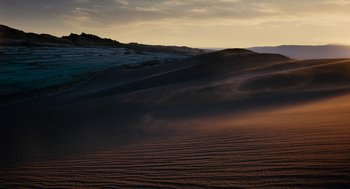 Movie still from “Voyage of Time” (2016), directed by Terrence Malick – A desert landscape with sand blowing in the wind; Extreme Wide shot, High angle