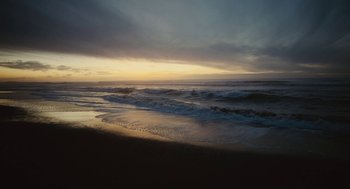 Movie still from “Voyage of Time” (2016), directed by Terrence Malick – The sun is setting over the ocean with waves crashing on the beach; Extreme Wide shot, High angle