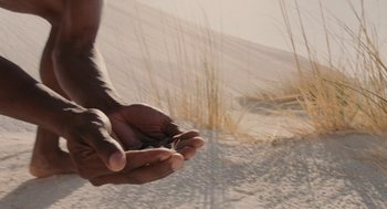Movie still from “Voyage of Time” (2016), directed by Terrence Malick – A person holding a piece of grass in their hands; Extreme Close Up shot, High angle