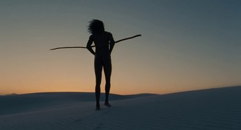 Movie still from “Voyage of Time” (2016), directed by Terrence Malick – A woman standing in the sand holding a stick; Wide shot, Low angle