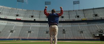 Movie still from “W.” (2008), directed by Oliver Stone – A man standing on a field with his hands raised; Wide shot, Low angle