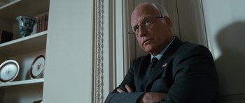 Movie still from “W.” (2008), directed by Oliver Stone – An older man wearing a suit and tie; Close Up shot, Over the shoulder angle