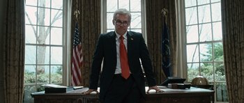 Movie still from “W.” (2008), directed by Oliver Stone – A man in a suit standing in front of two flags; Medium shot, Low angle