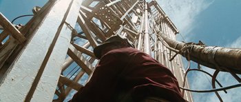 Movie still from “W.” (2008), directed by Oliver Stone – A man standing next to a tall wooden structure; Wide shot, Low angle