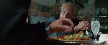 Movie still from “W.” (2008), directed by Oliver Stone – An older man sitting at a table with a plate in front of him; Close Up shot, Over the shoulder angle