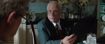 Movie still from “W.” (2008), directed by Oliver Stone – An older man sitting at a table looking at a cell phone; Close Up shot, Over the shoulder angle