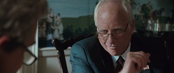 Movie still from “W.” (2008), directed by Oliver Stone – An older man wearing glasses and a suit; Close Up shot, Over the shoulder angle