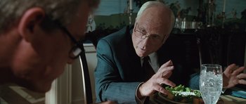 Movie still from “W.” (2008), directed by Oliver Stone – An older man in a suit and glasses looking at a plate of food; Close Up shot, Over the shoulder angle