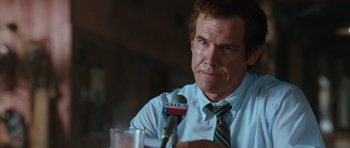 Movie still from “W.” (2008), directed by Oliver Stone – A person sitting at a table holding a microphone; Close Up shot, Low angle