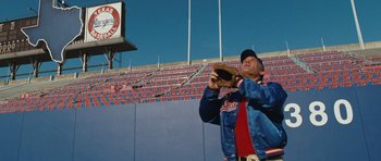 Movie still from “W.” (2008), directed by Oliver Stone – A man holding a baseball glove in front of an empty stadium; Wide shot, Low angle