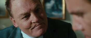 Movie still from “W.” (2008), directed by Oliver Stone – An older man wearing a suit and tie looking at the camera; Close Up shot, Over the shoulder angle