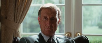 Movie still from “W.” (2008), directed by Oliver Stone – An older man wearing a suit and tie in front of a window; Close Up shot, Low angle