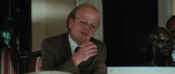 Movie still from “W.” (2008), directed by Oliver Stone – A man in a suit and glasses talking to someone; Close Up shot, Over the shoulder angle